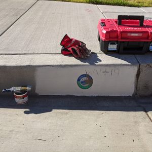 Red craftsman toolbox of paint and supplies sitting on a curb over a storm drain that was previously covered in graffiti
